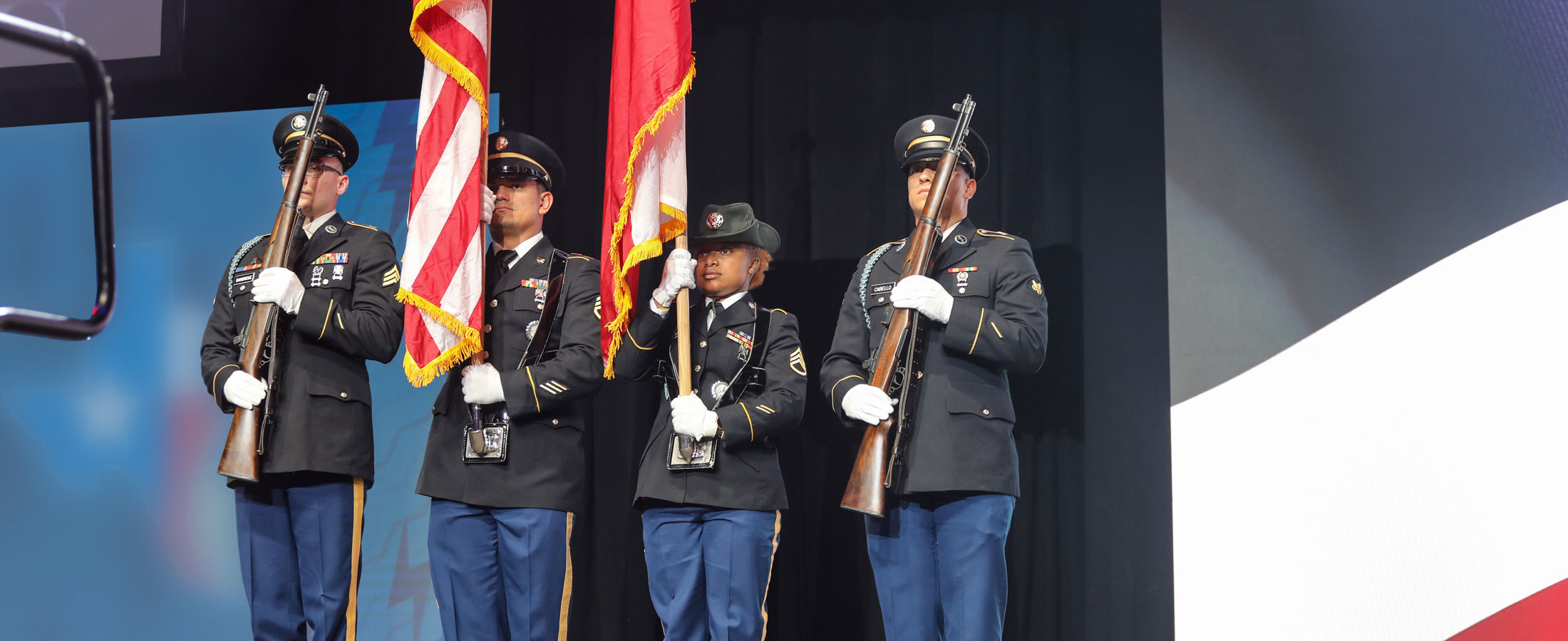 Cuatro militares están de pie presentando la bandera estadounidense y la bandera de Texas.